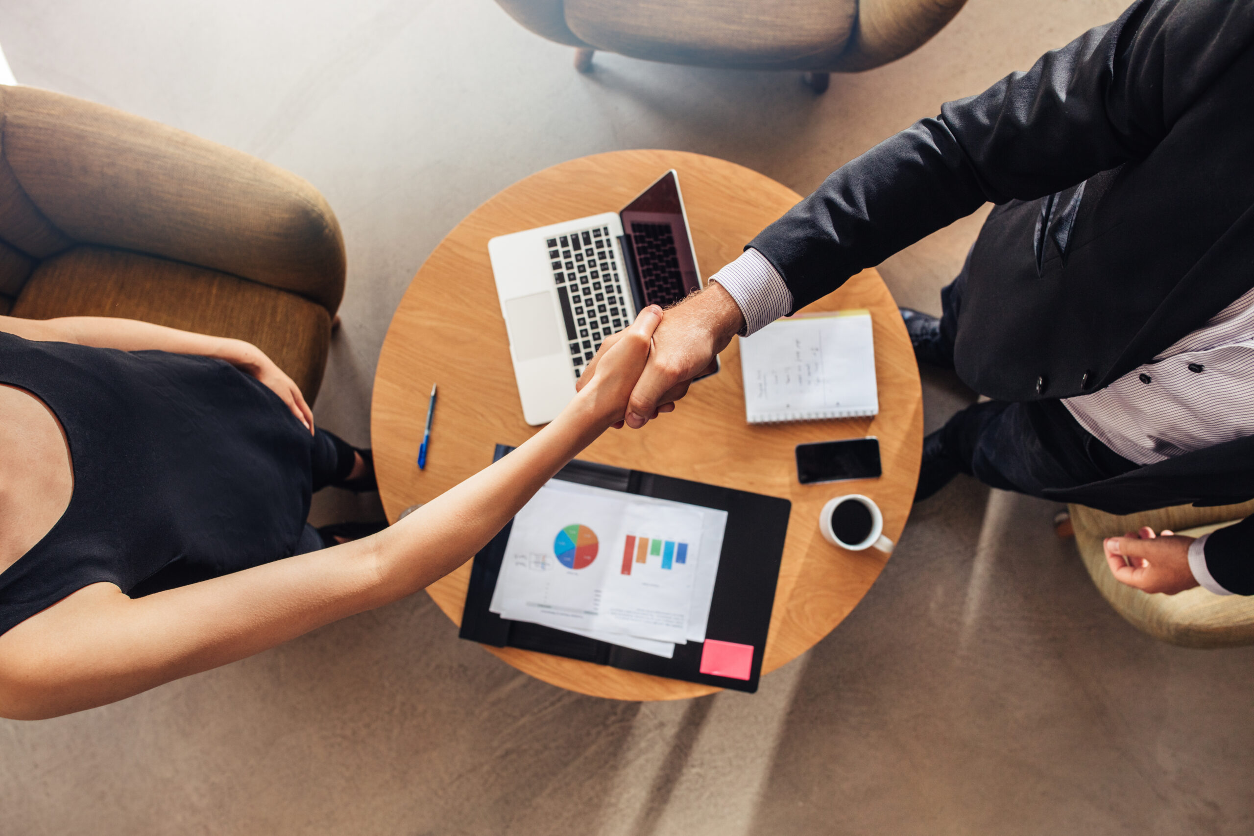 Top view of young business partners shaking hands over deal at office. Focus on hand shake.