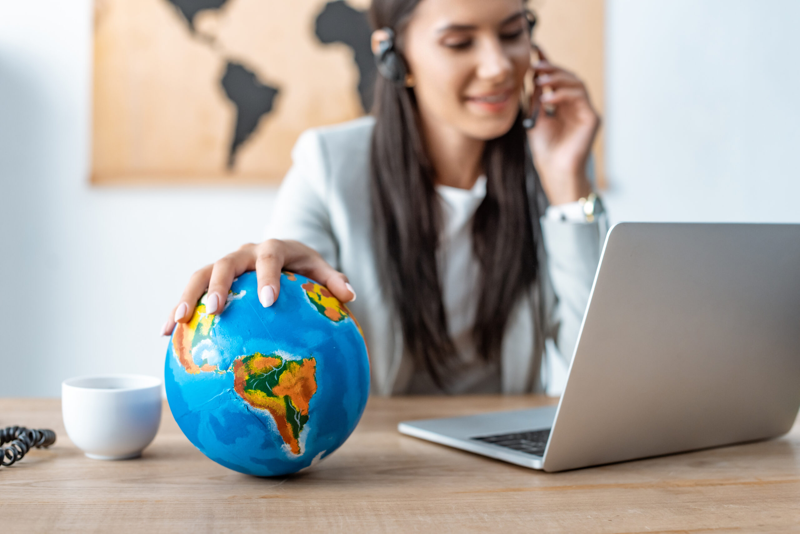 selective focus of travel agent holding hand on globe while working at workplace